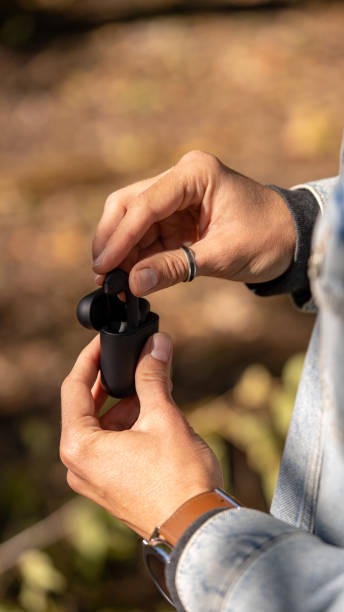 istock Black wireless bluetooth earphones or headphones, plastic case or box for storage and charging and smartphone on wooden background, close up 1346211897