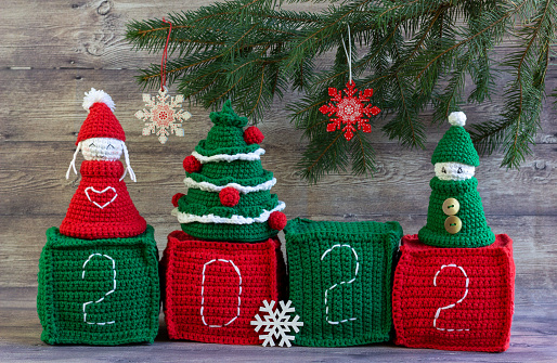 Creative New Year's composition with knitted toys, cubes 2020, snowflakes, a branch of a Christmas tree on a wooden background. Greeting card. Winter holiday season, Christmas time concept.
