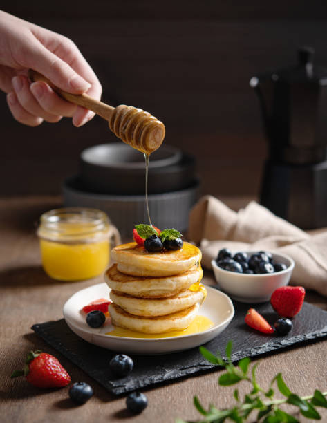 istock A hand pours honey on classic American pancakes in a stack with fresh berries on a blurry brown background. The concept of a healthy, delicious and nutritious breakfast 1346221867