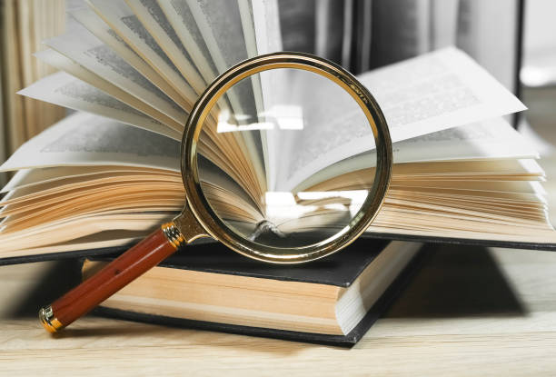 렌즈를 돋보이게 하고 나무 테이블에 페이지를 돌리는 오픈 및 폐쇄 된 책. 정보 개념 읽기 및 찾기 - legal system law book dictionary 뉴스 사진 이미지