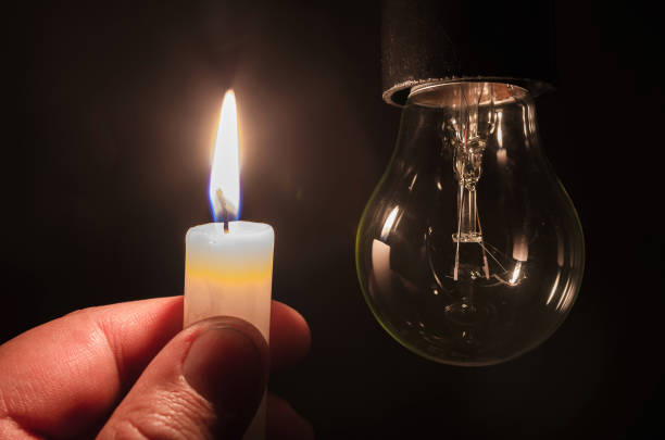 Burning candle near a switched off light bulb in complete darkness. stock photo