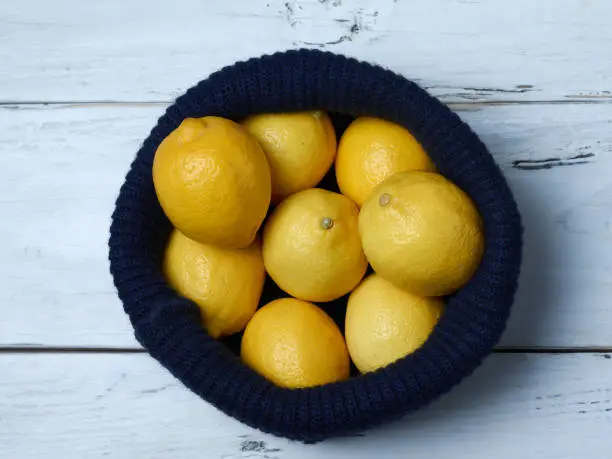 top view of yellow lemons inside a blue wool cap on a white wooden table.