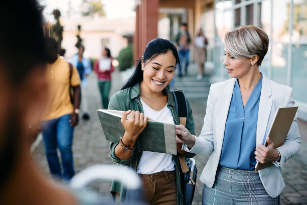 University teacher talking to her Asian female student at campus. Happy Asian student communicating with her professor in front of university building. lecturer stock pictures, royalty-free photos & images