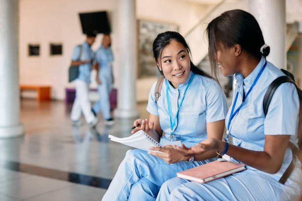 asian nursing student and her female friend talking while studying in hallway at medical university. - medical student healthcare and medicine book education imagens e fotografias de stock