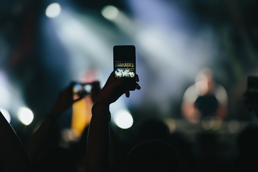 Fan in an audience on a concert recording on his smartphone live act of a musician on a festival
