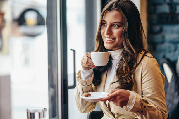 istock Woman using a smartphone and drinking coffee while sitting in a coffee shop 1346228973