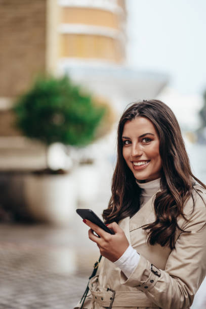 istock Beautiful young woman using a smartphone while out in the city 1346228974