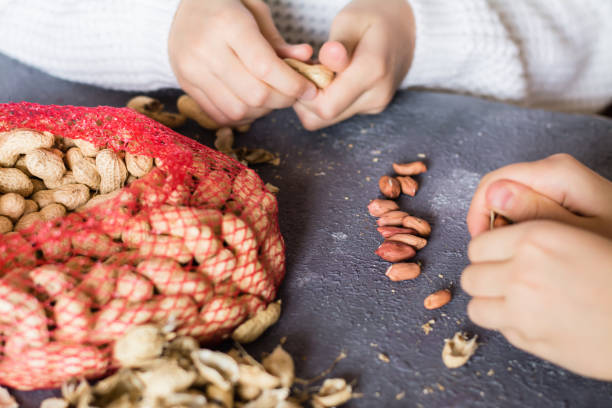 istock Peanut kernels, a mesh bag with unpeeled nuts and husks on the table. Children's hands are peeling nuts. Lifestyle 1346232436