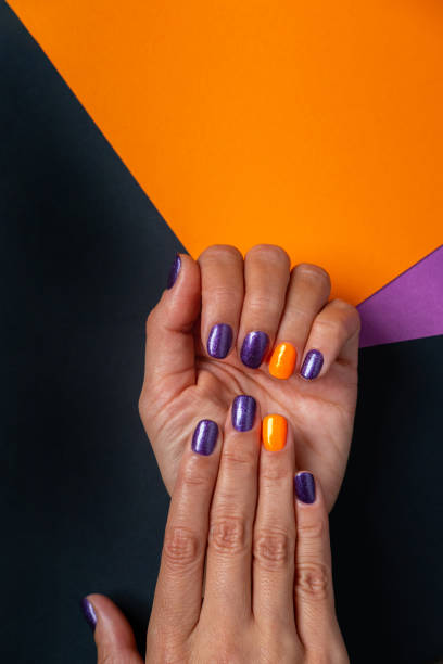 Halloween violet permanent manicure on black, orange and violet background, place for text above. Autumn trendy violet and orange female gel manicure. Woman's hands with violet permanent manicure on black, violet and orange background. fall nail art stock pictures, royalty-free photos & images