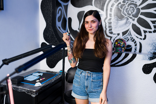 Portrait of a cheerful young woman looking at the camera and feeling satisfied with her new tattoo at the art studio