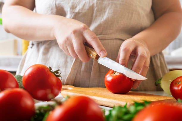 istock Chef slicing tomato using knife on the table in restaurant. Process of cutting and preparation food in kitchen. 1346236134