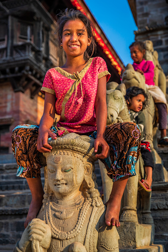 Little girls sitting on a horse sculpture, Siddhi Lakshmi Shikara Hindu temple in the Durbar square of Bhaktapur. Bhaktapur is an ancient town in the Kathmandu Valley and is listed as a World Heritage Site by UNESCO for its rich culture, temples, and wood, metal and stone artwork.