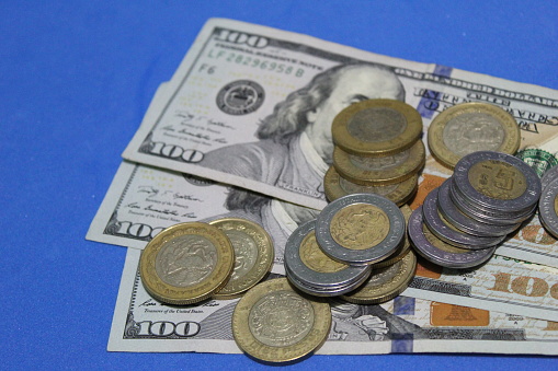 stacked mexican coins and American banknotes of 100 dollars