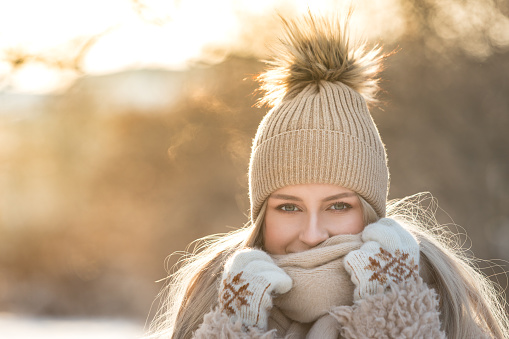 Happy woman enjoy sunny winter weather. Closeup outdoor portrait of cute female on walk in snowy park wearing wintertime clothes, wool scarf, hat and mittens with snowflakes. Christmas season concept