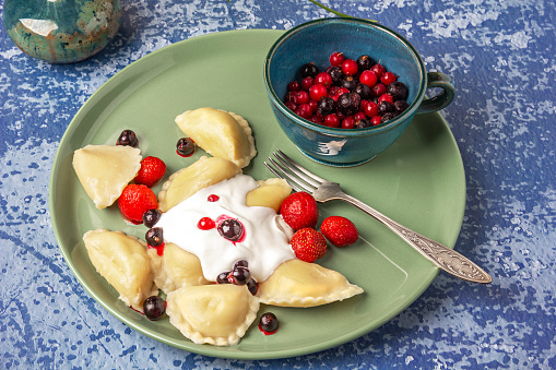 Pierogi stuffed with curd served with sour cream, strawberries, black and red currants.