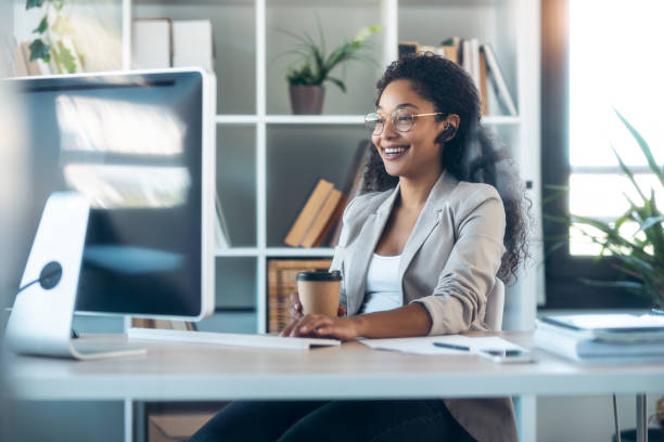 istock Elegant business woman working with computer while talking with earphone sitting in modern startup office. 1346245411