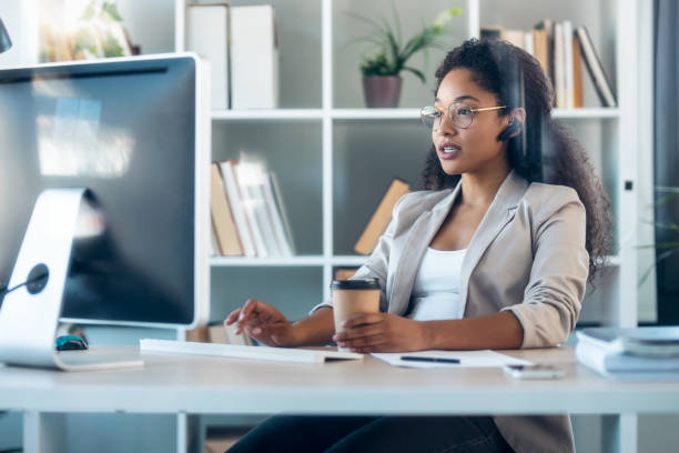 istock Elegant business woman working with computer while talking with earphone sitting in modern startup office. 1346245579