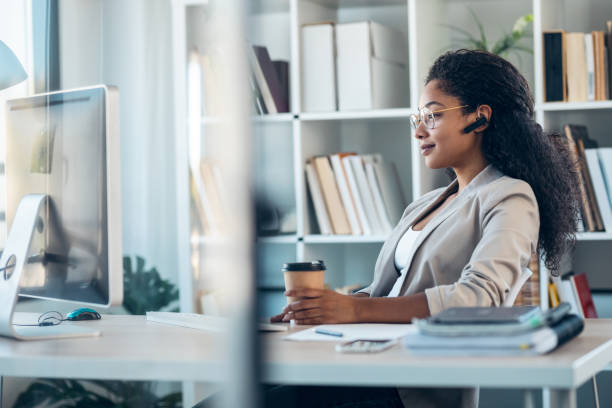 istock Elegant business woman working with computer while talking with earphone sitting in modern startup office. 1346245720