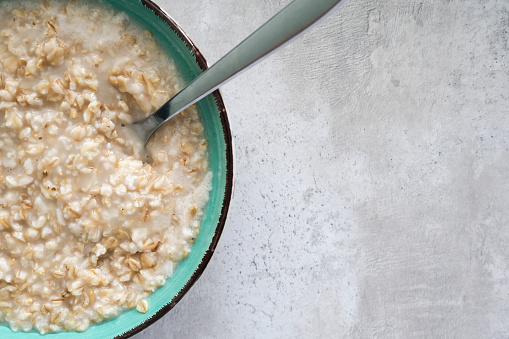 A green bowl of cooked oats porridge with a spoon, healthy breakfast and dieting product close up with copy space.