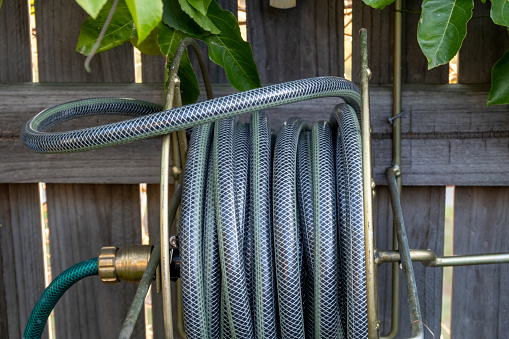 A rolled up hose on a reel in a garden with a timber fence background