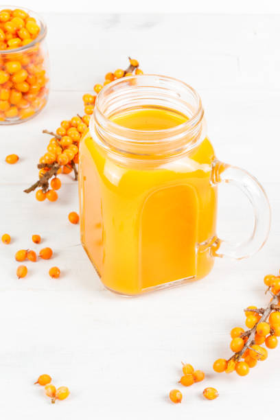 Yellow juice in a glass mug. Close-up on a white background, with sea buckthorn twigs. stock photo