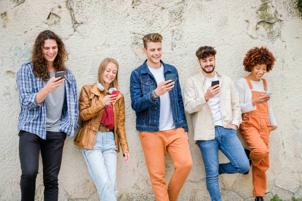 istock Multicultural group of friends using cellphones outdoors - Students browsing internet holding mobile smart phones standing beside wall 1346249163