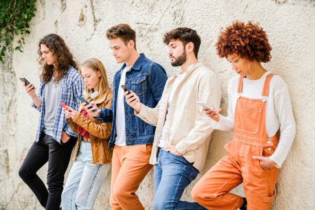 istock Multicultural group of friends using cellphones outdoors - Students browsing internet holding mobile smart phones standing beside wall 1346249195