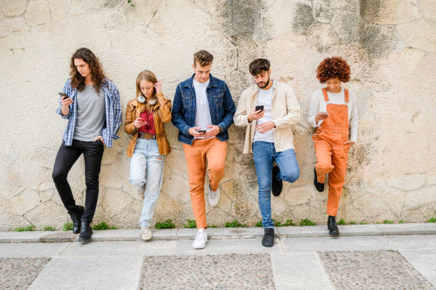 istock Multicultural group of friends using cellphones outdoors - Students browsing internet holding mobile smart phones standing beside wall 1346249216