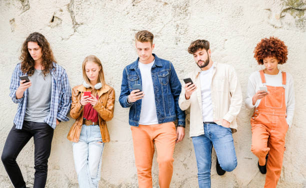 istock Multicultural group of friends using cellphones outdoors - Students browsing internet holding mobile smart phones standing beside wall 1346249246
