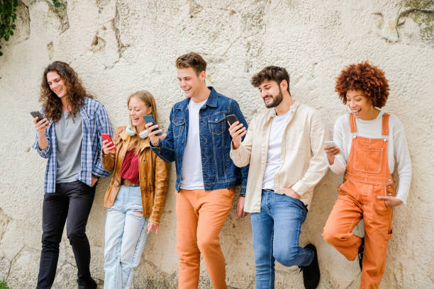 istock Multicultural group of friends using cellphones outdoors - Students browsing internet holding mobile smart phones standing beside wall 1346249273