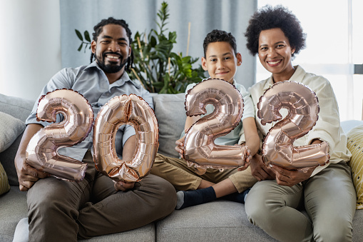 Married couple with their son sitting on the couch, holding 2022 balloons, looking at camera and smiling
