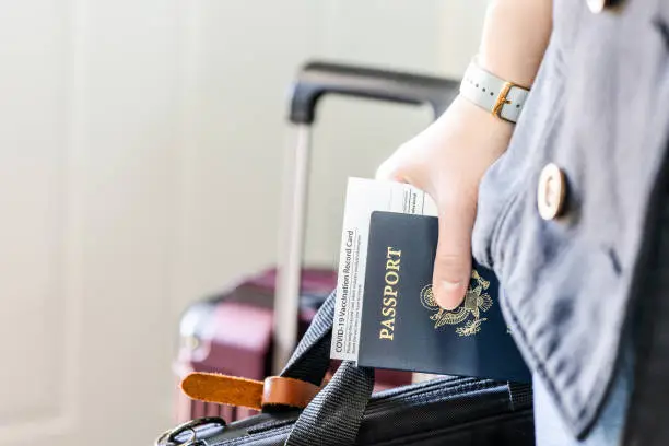 Hand holding passport and approved vaccination card with laptop bag ready for business trip. Vaccine and citizen identity documents of passenger require for travel in new normal.