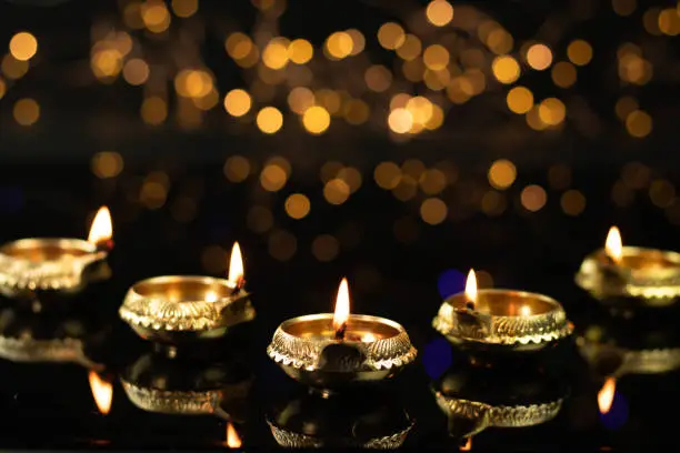 Golden Brass Diya Illuminated With Reflection In Dark Black Background With Bokeh Effect. Indian Festival Theme For Diwali Pooja, Navratri, Dussehra Puja, New Year, Deepawali Or Shubh Deepavali