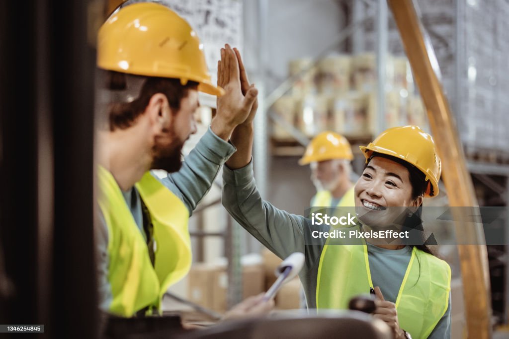 We really do achieve more when we stand together Shot of happy and successful warehouse colleagues giving high five Warehouse Stock Photo