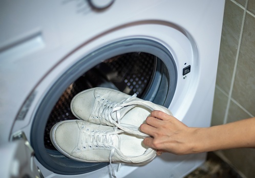 Woman hand putting pair of sport shoes into washing machine, closeup