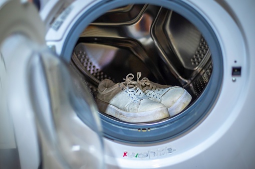 Footwear hygiene. Pair of dirty white sneakers in the washing machine