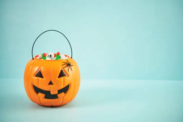 Photo of Jack O'Lantern Halloween Bucket Filled with Candy on Blue Background