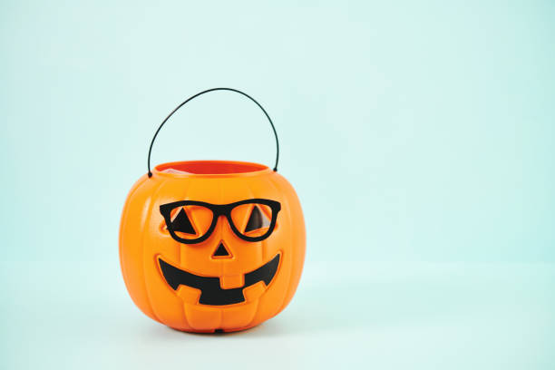 istock Jack O'Lantern Halloween Bucket Wearing Eyeglasses against a Blue Background 1346279027