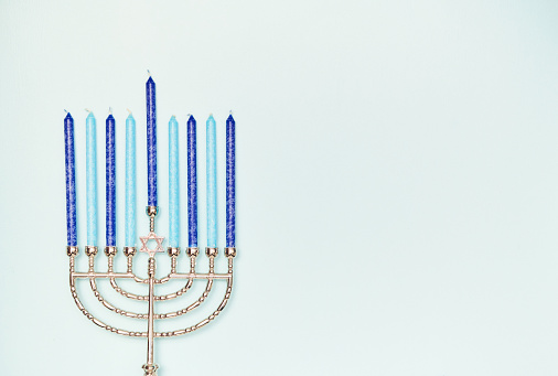Hanukkah menorah symbol or Chanukah candlestick with lit candles as a seasonal traditional faith symbol on a white background as a 3D illustration.