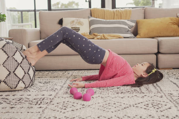 istock Mixed Asian girl doing Glute Bridge exercising at home, using zoom online virtual workout class , social distancing, homeschooling, remotely learning during covid pandemic, new normal concept 1346285310