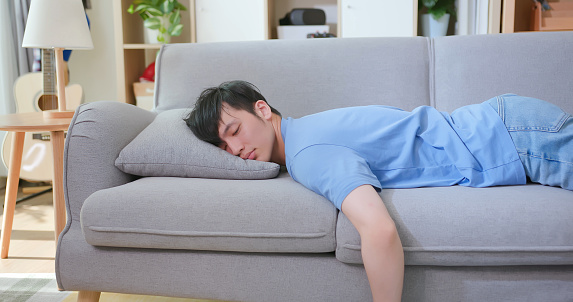 asian man lying buried his face in couch feels tired in living room at home