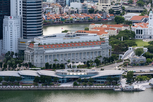 The iconic Fullerton Hotel seen in the Marina Bay area of Singapore. Seen in the afternoon. In front the Fullerton Bay waterfront promenade which is full of restaurants and shops.