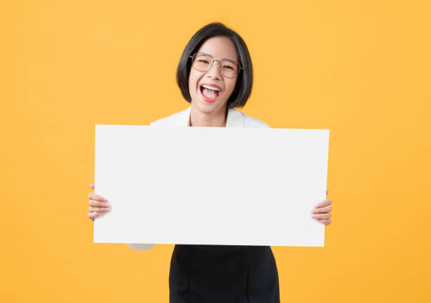Young Asian woman holding blank paper with smiling face and looking on the orange background. for advertising signs. stock photo