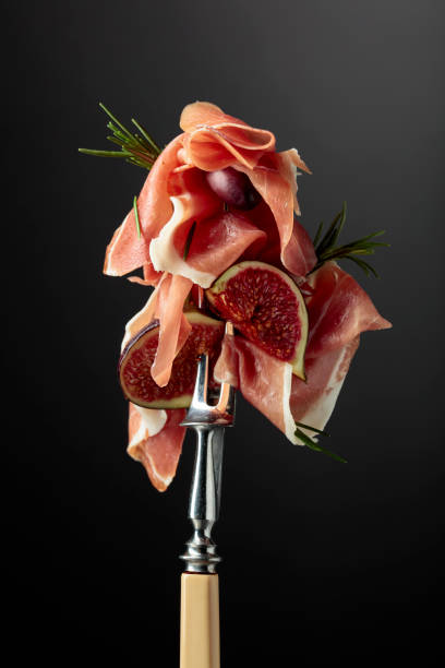 istock Prosciutto with figs, rosemary, and red olives on a fork. 1346298711
