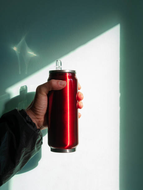 istock Red thermo can bottle in male hands against wall with harsh shadow.Hot tea coffee drinking in cold autumn winter weather 1346306236