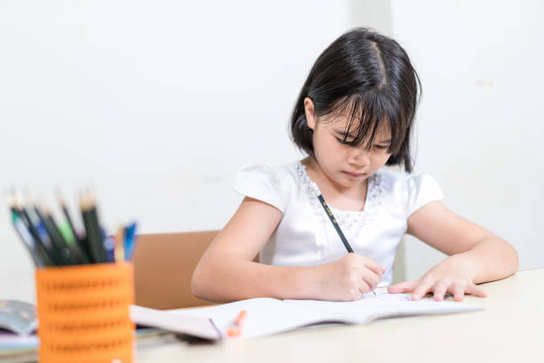 istock Cheerful Asian little girl children student writing on notebook doing homework and self study at home 1346308368