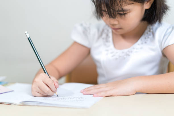 istock Cheerful Asian little girl children student writing on notebook doing homework and self study at home 1346308492