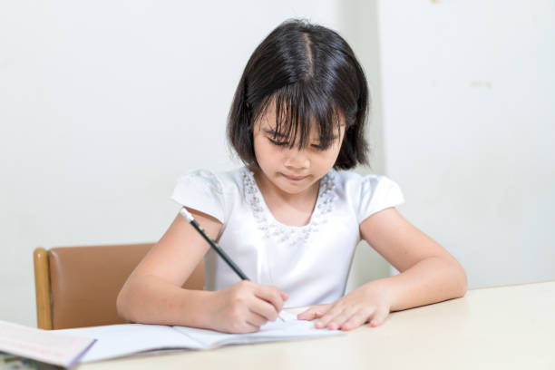 istock Cheerful Asian little girl children student writing on notebook doing homework and self study at home 1346308566