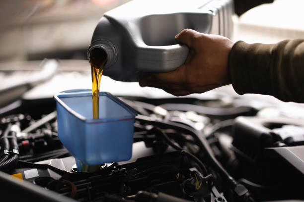 Foreman pours car oil into engine through watering can closeup Foreman pours car oil into engine through watering can. Engine oil change intervals concept intermission stock pictures, royalty-free photos & images