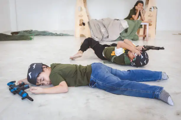 Photo of Group of Asian soldier children with toy machine gun in army camouflage crawling and playing on floor